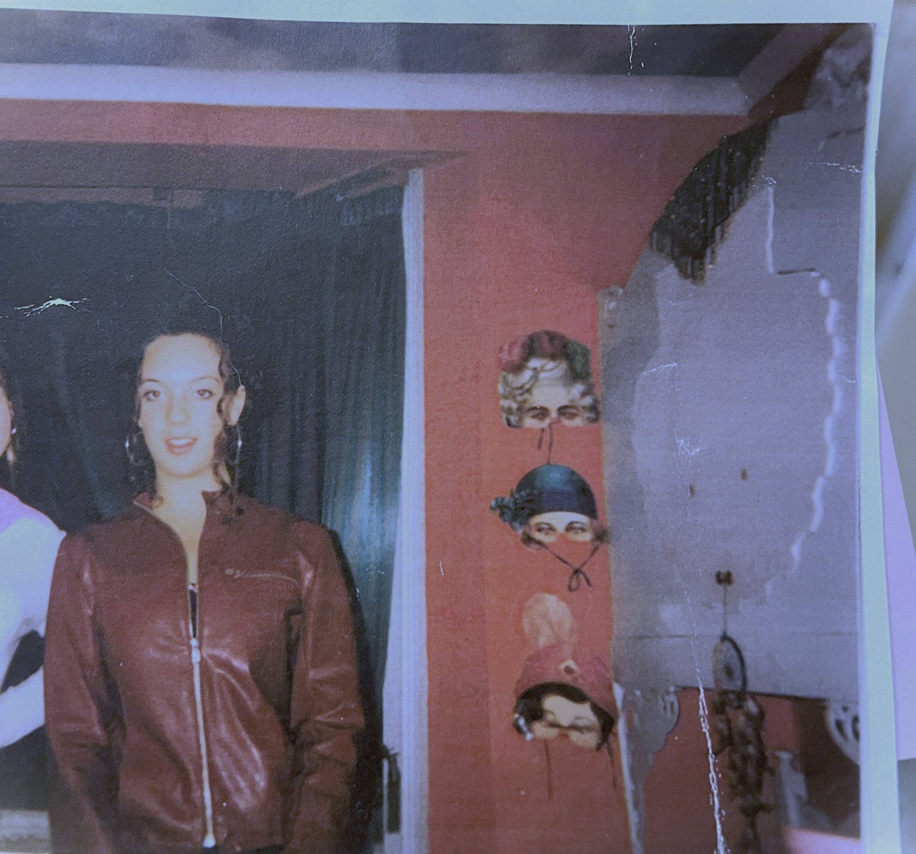 An early photograph of Camilla in a leather jacket in front of a theatre set with masks on the wall