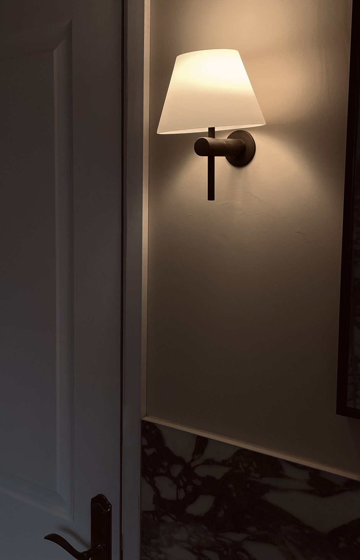 A brass swing-arm wall light with a pleated linen shade beside a dark door