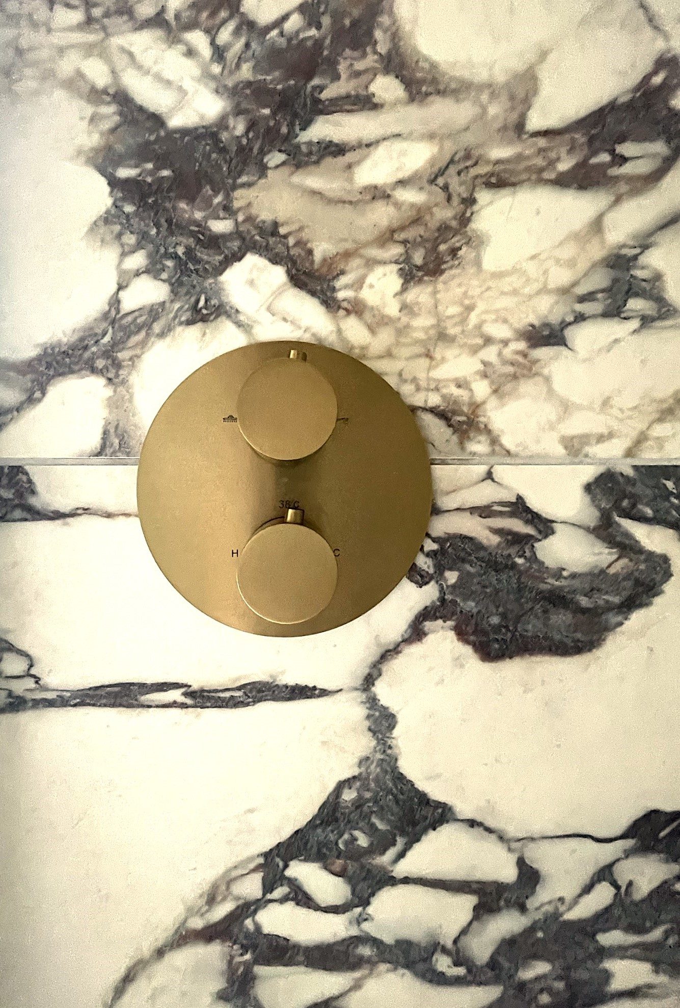 A round brushed brass shower control set into marble