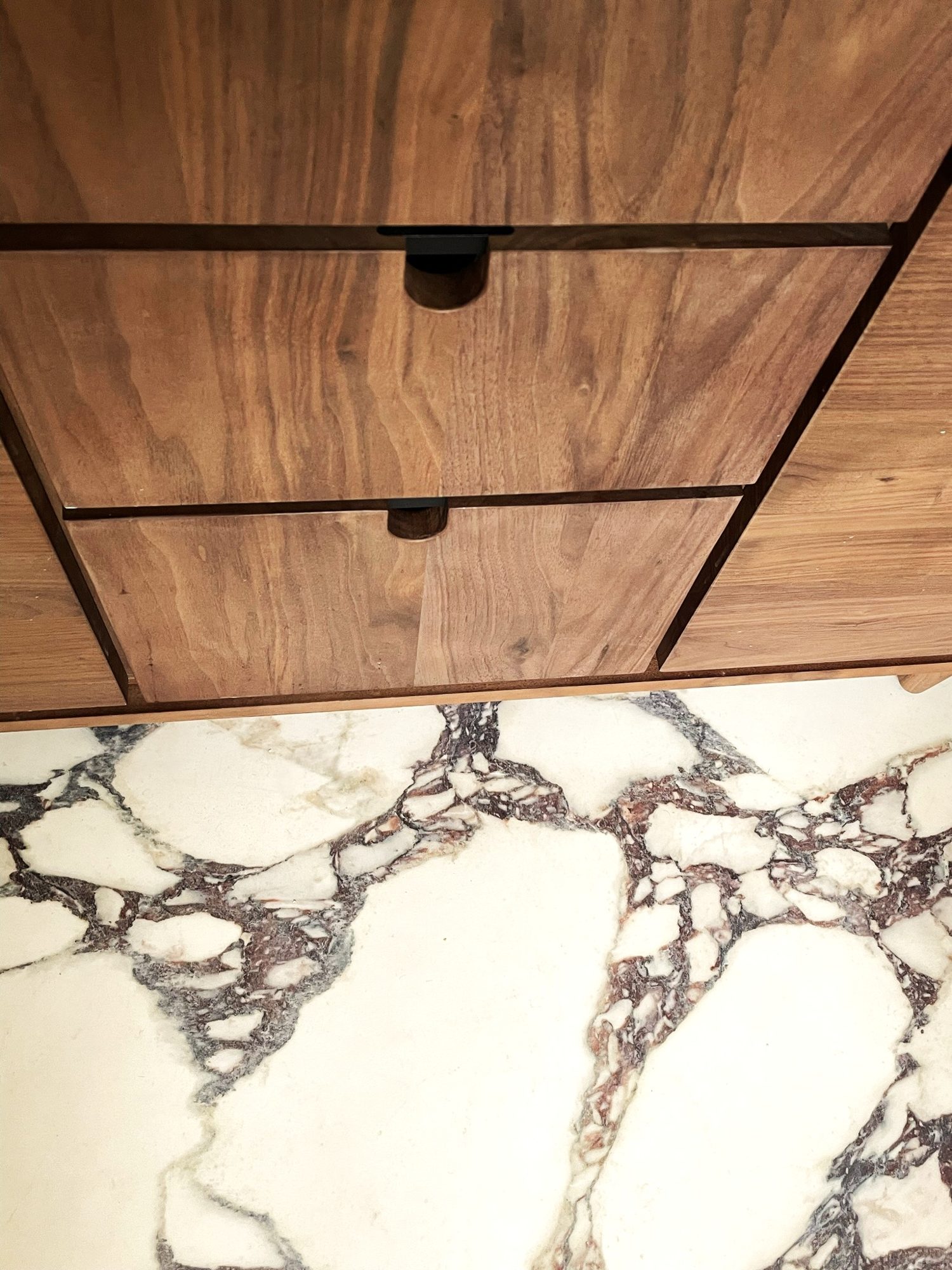 Walnut vanity drawers with recessed black pulls above a marble floor