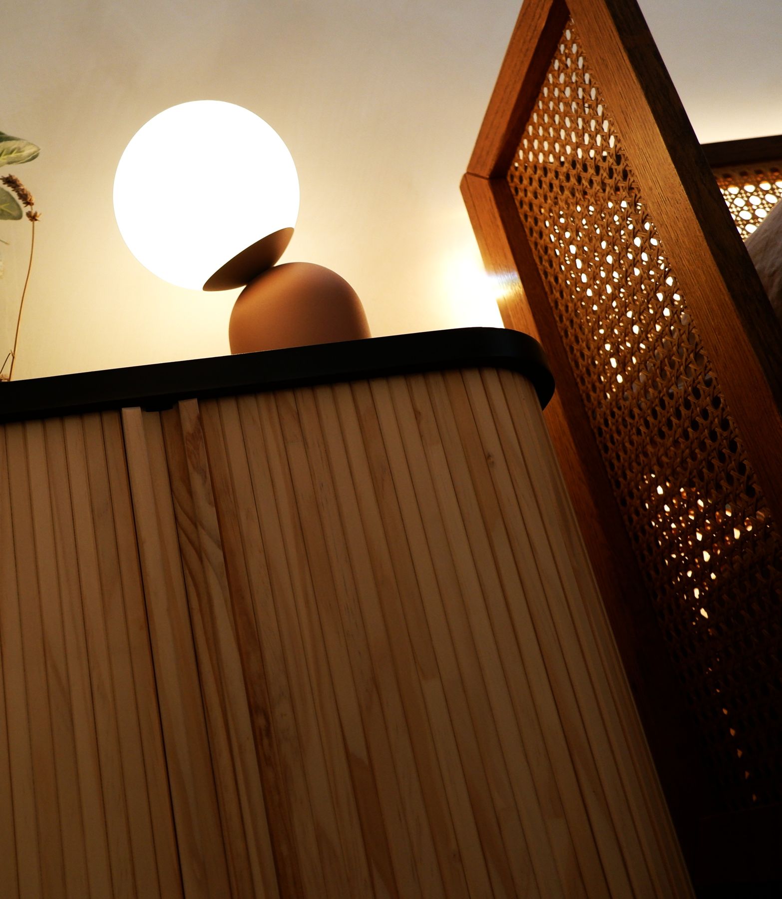 A globe lamp on a ribbed wooden bedside table beside a cane screen