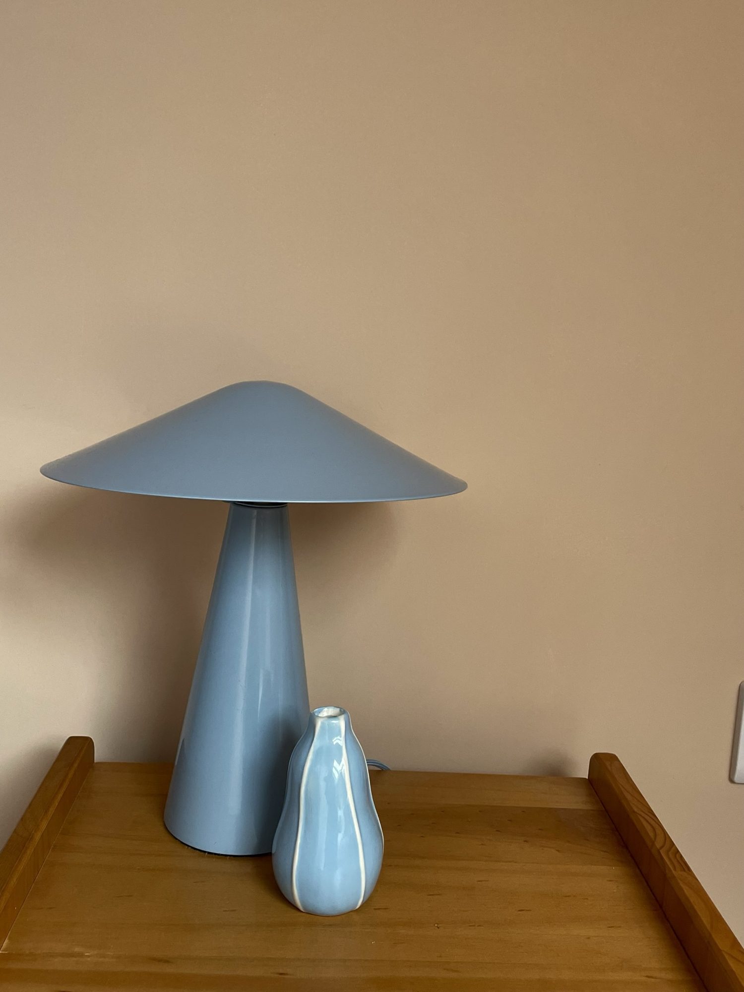 A powder-blue mushroom lamp and small vase on a wooden bedside table