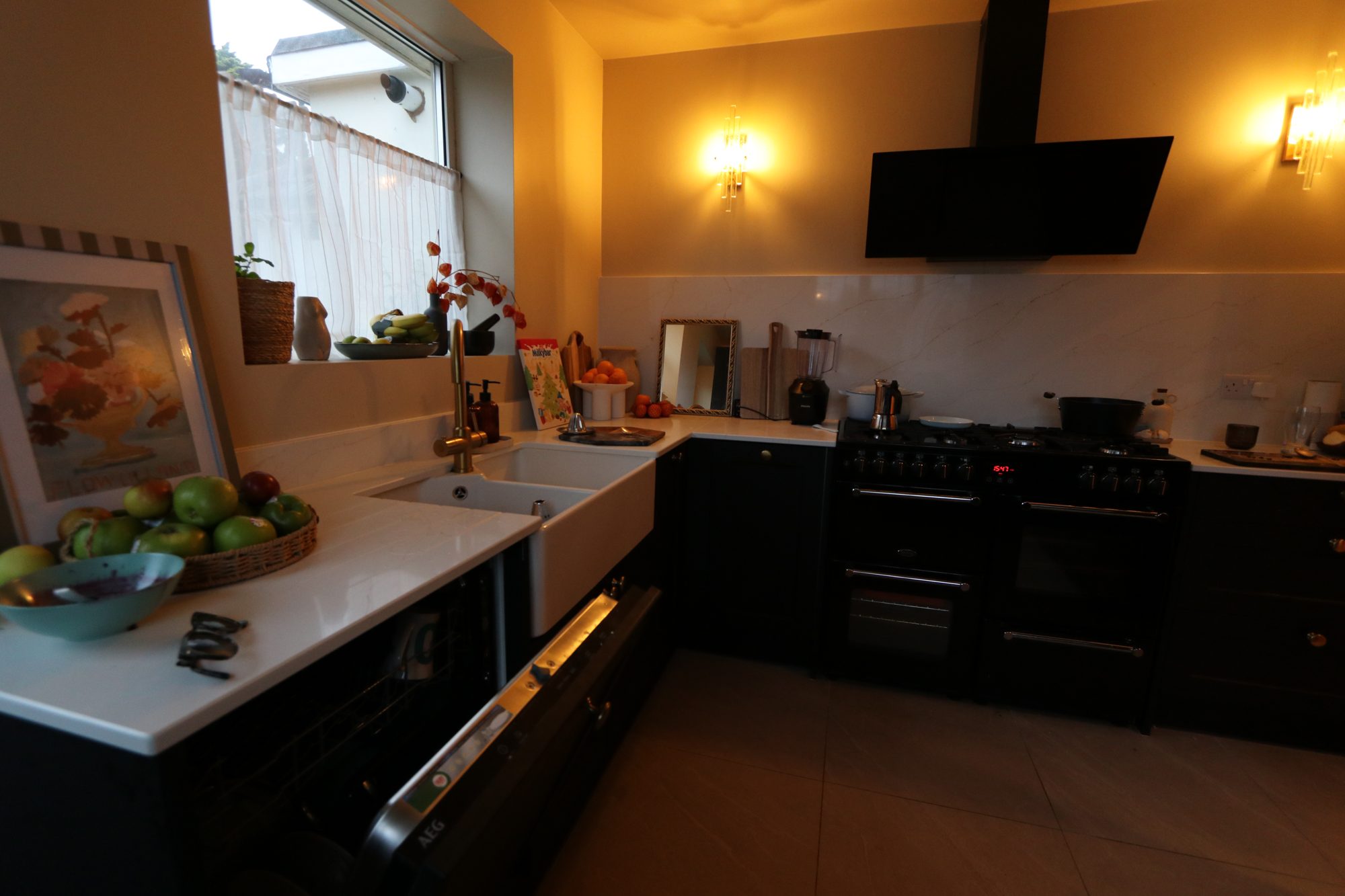 A dark-cabinet kitchen with a butler sink, range cooker and warm wall lights
