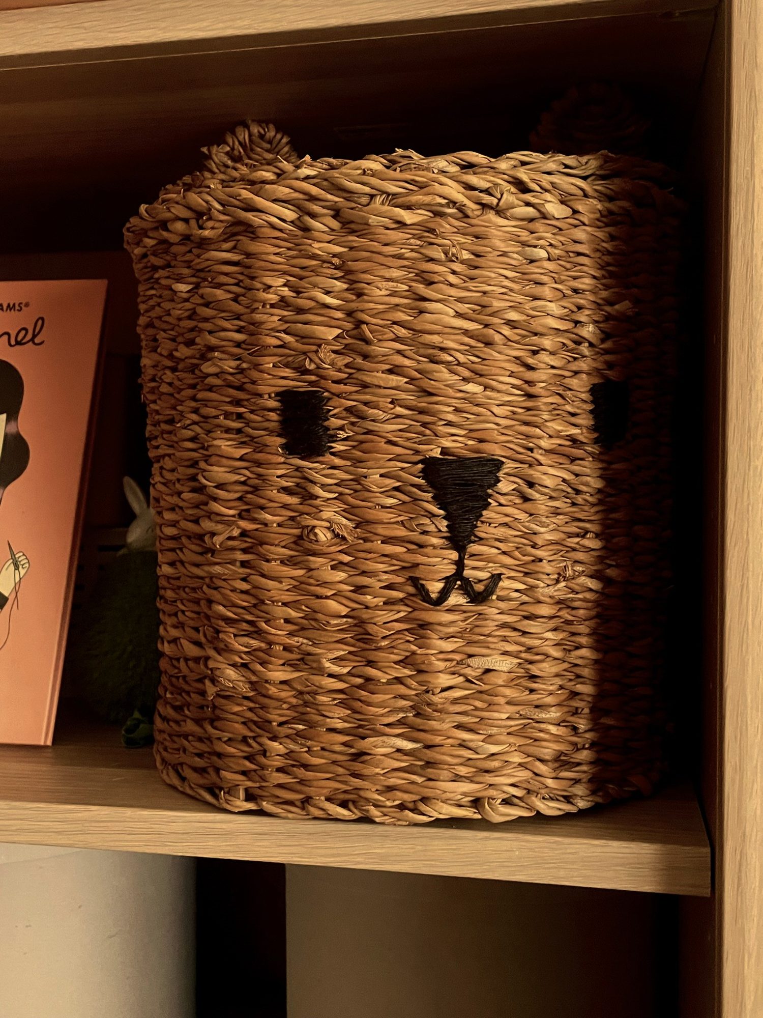 A woven seagrass storage basket with a bear face on a wooden shelf