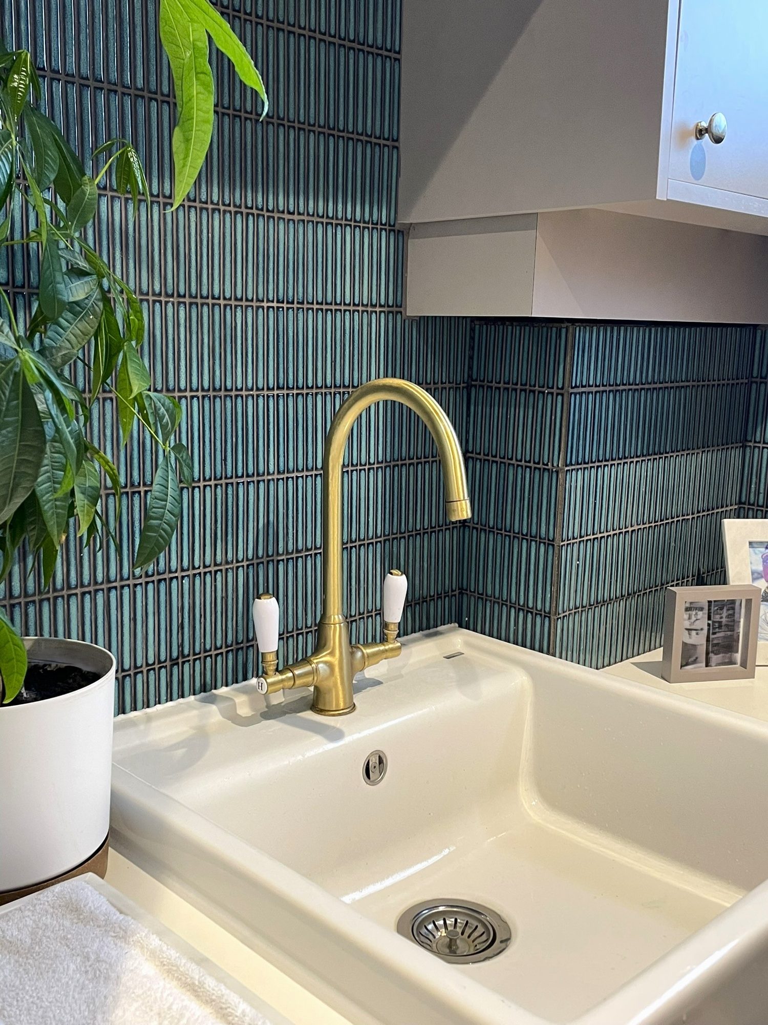 A white ceramic sink with a brass swan-neck tap against teal vertical tiles