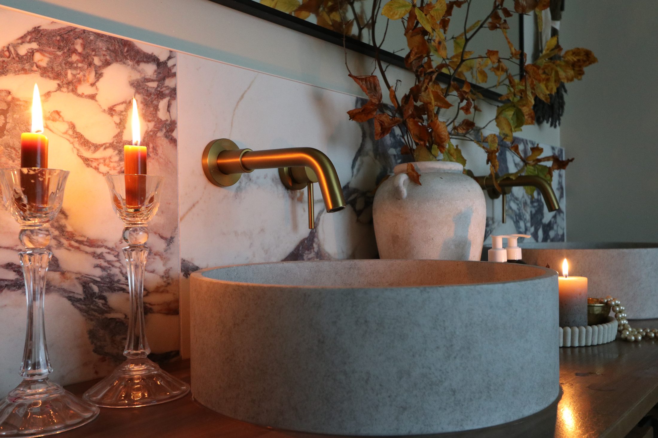 Lit candles in cut-glass holders beside a stone basin and brass tap