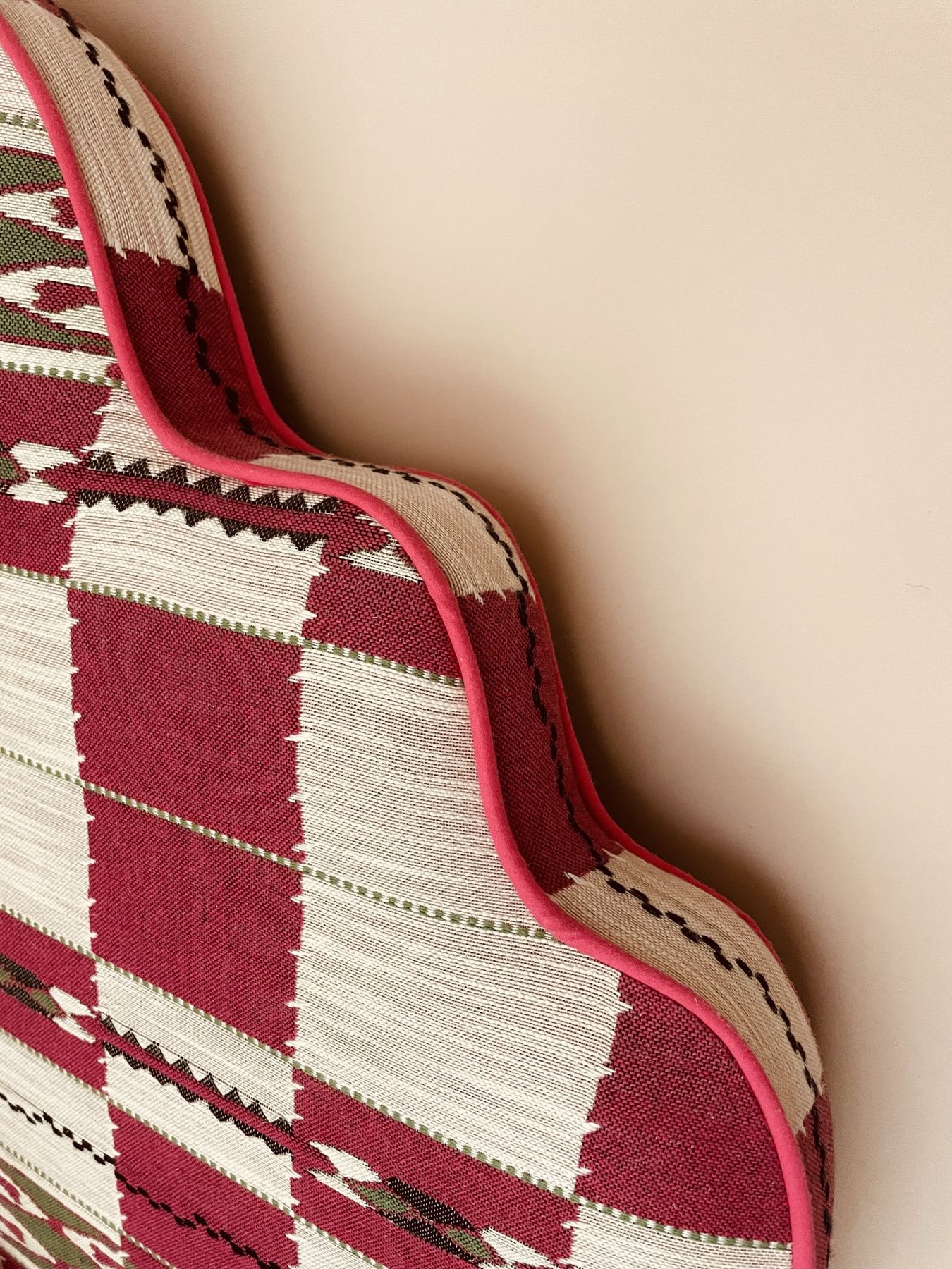 A scalloped headboard in red, cream and green woven fabric with pink piping