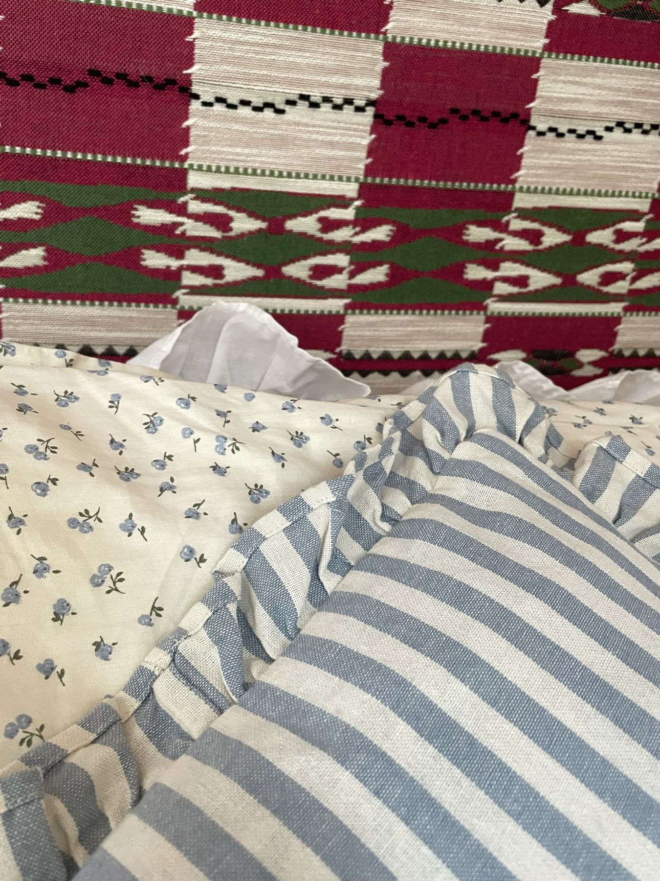 Ruffled pillows in blue stripes and ditsy florals against the woven headboard
