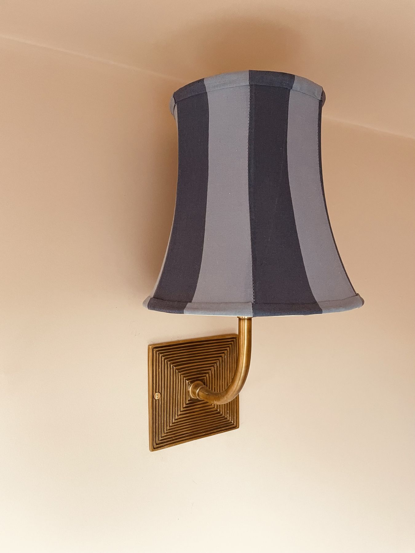 A brass wall light with a striped grey shade on a peach wall