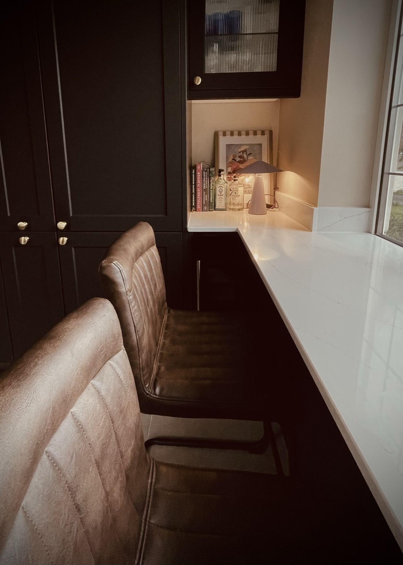 Brown leather bar stools at a pale stone breakfast bar beside dark cabinets