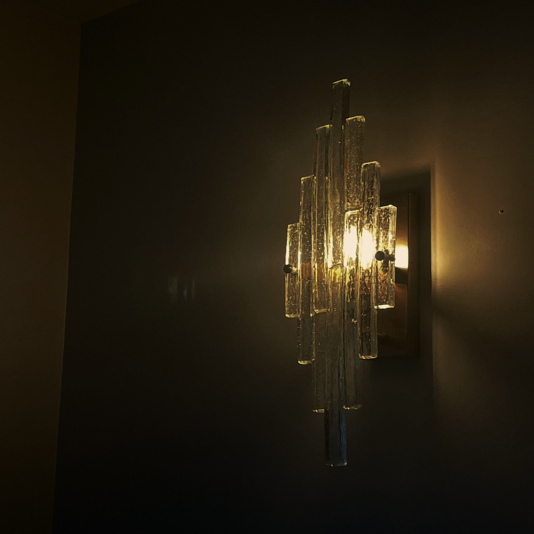 A glass wall light glowing against a dark painted wall
