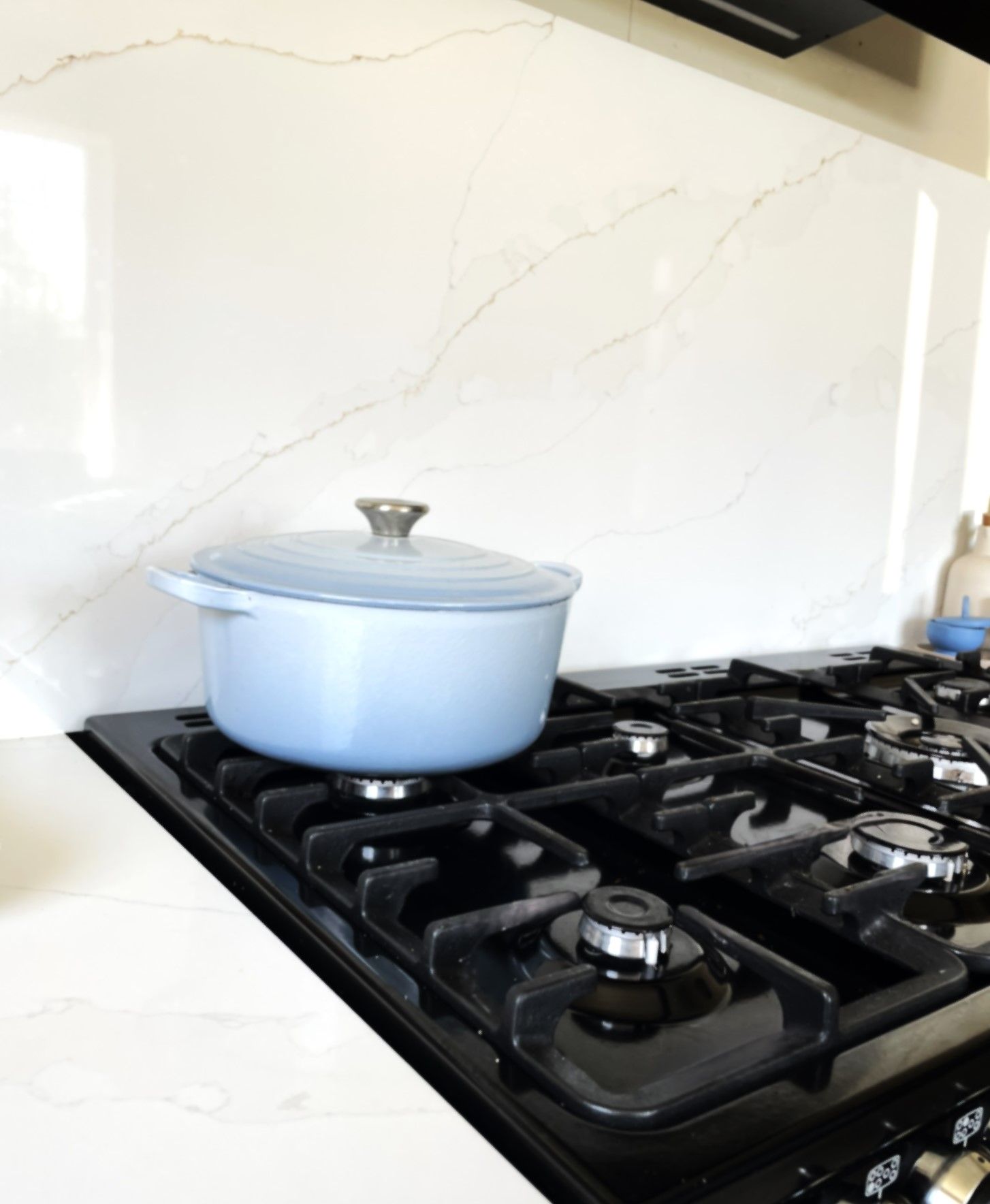 A pale blue cast-iron casserole on a black gas hob against marble-effect splashback