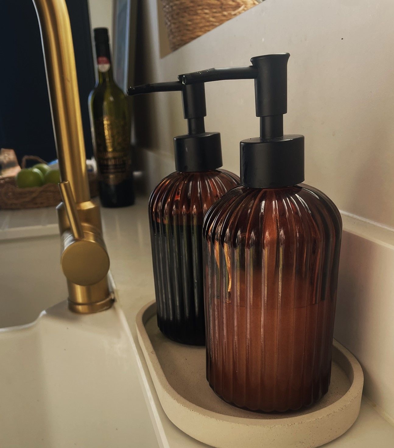 Amber ribbed soap bottles on a stone tray beside a brass tap