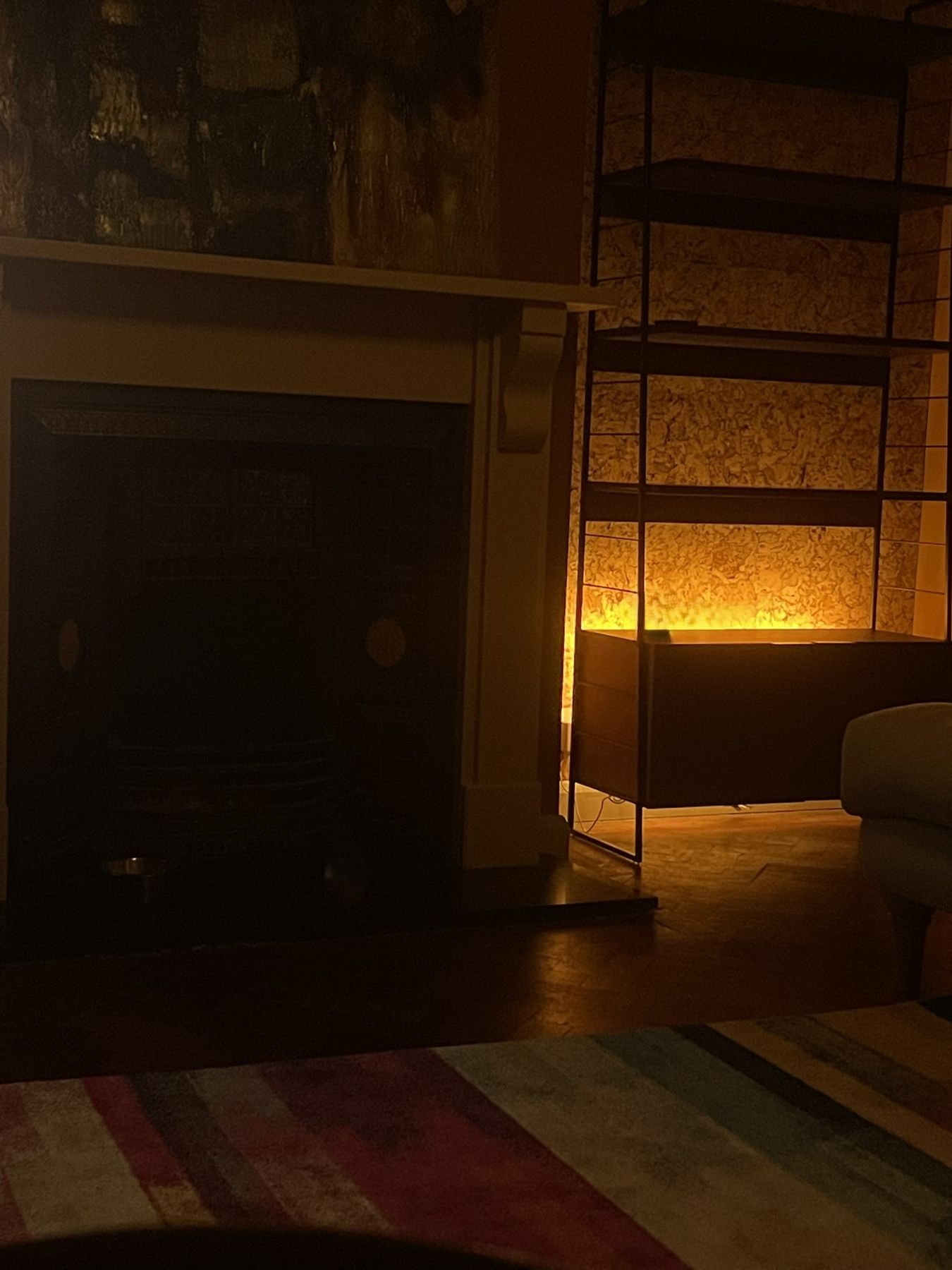 The fireplace and shelving at dusk, with a striped rug in the foreground