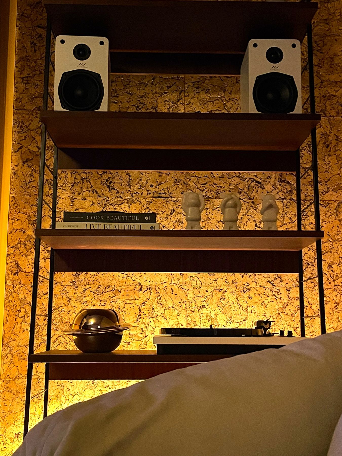 Black string shelving against cork, holding speakers, records and a turntable