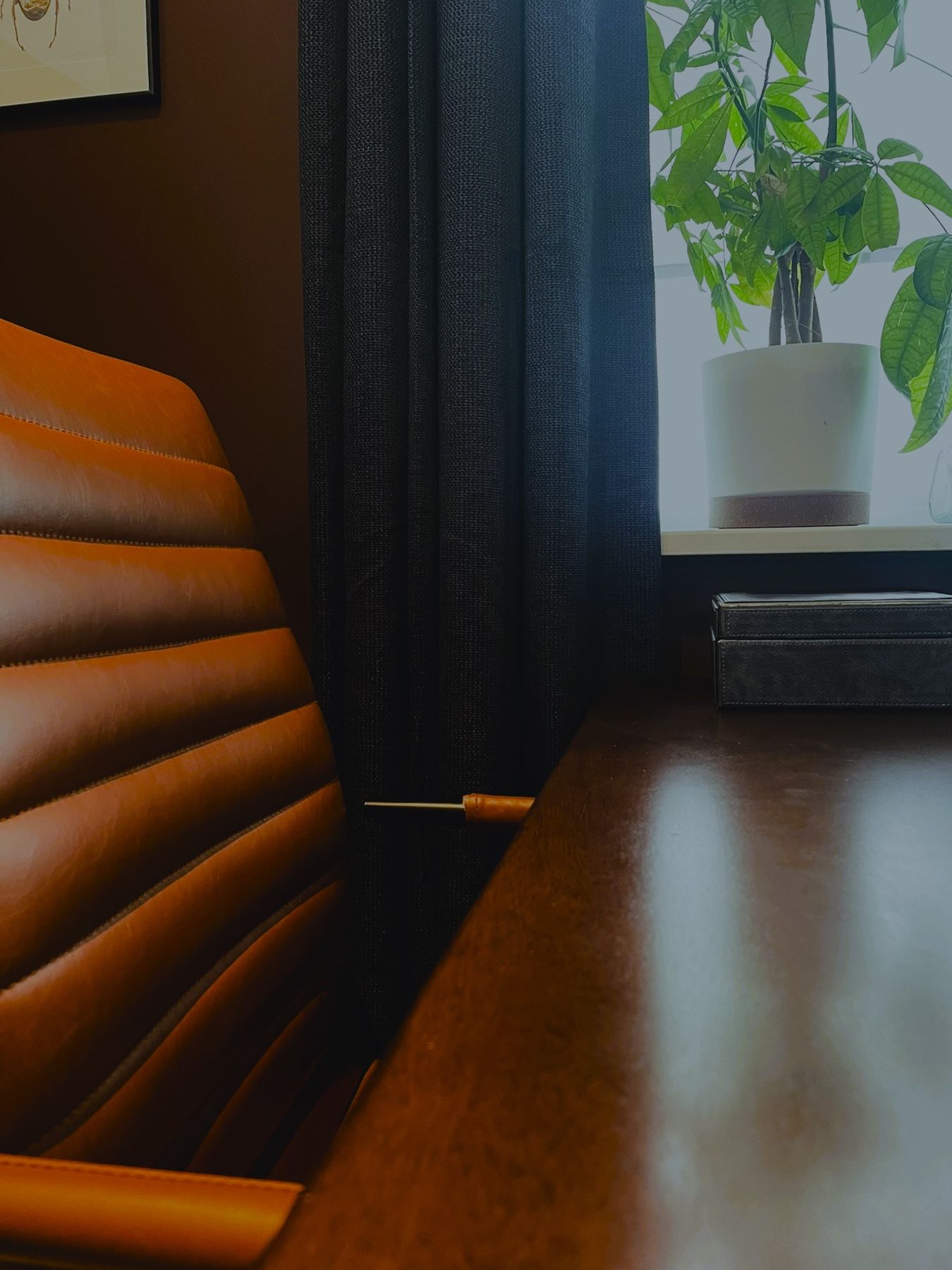 A ribbed tan leather chair at a dark wood desk by a window