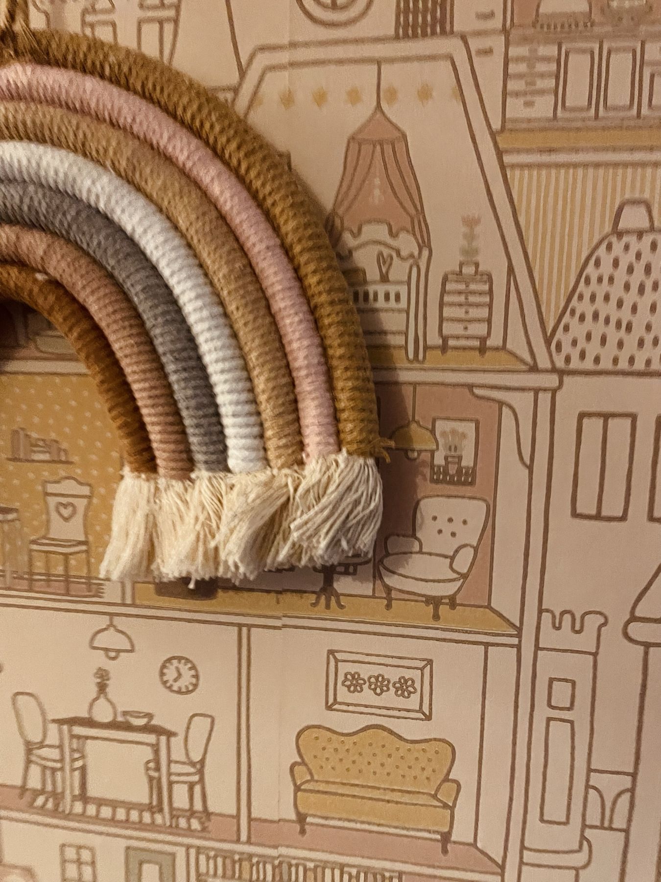 A macramé rainbow wall hanging against townhouse wallpaper