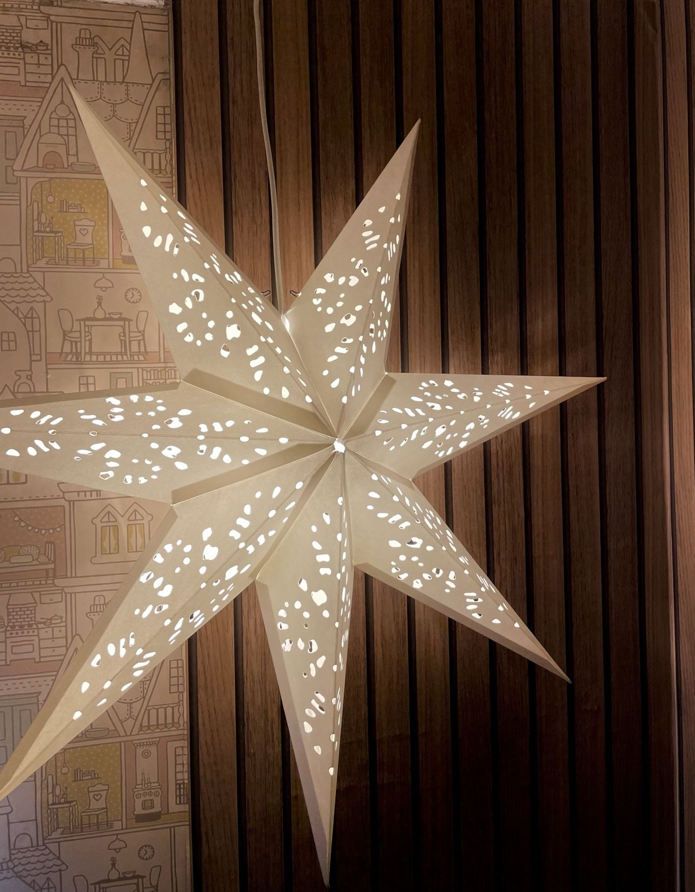 A white paper star lantern hanging against dark slatted panelling
