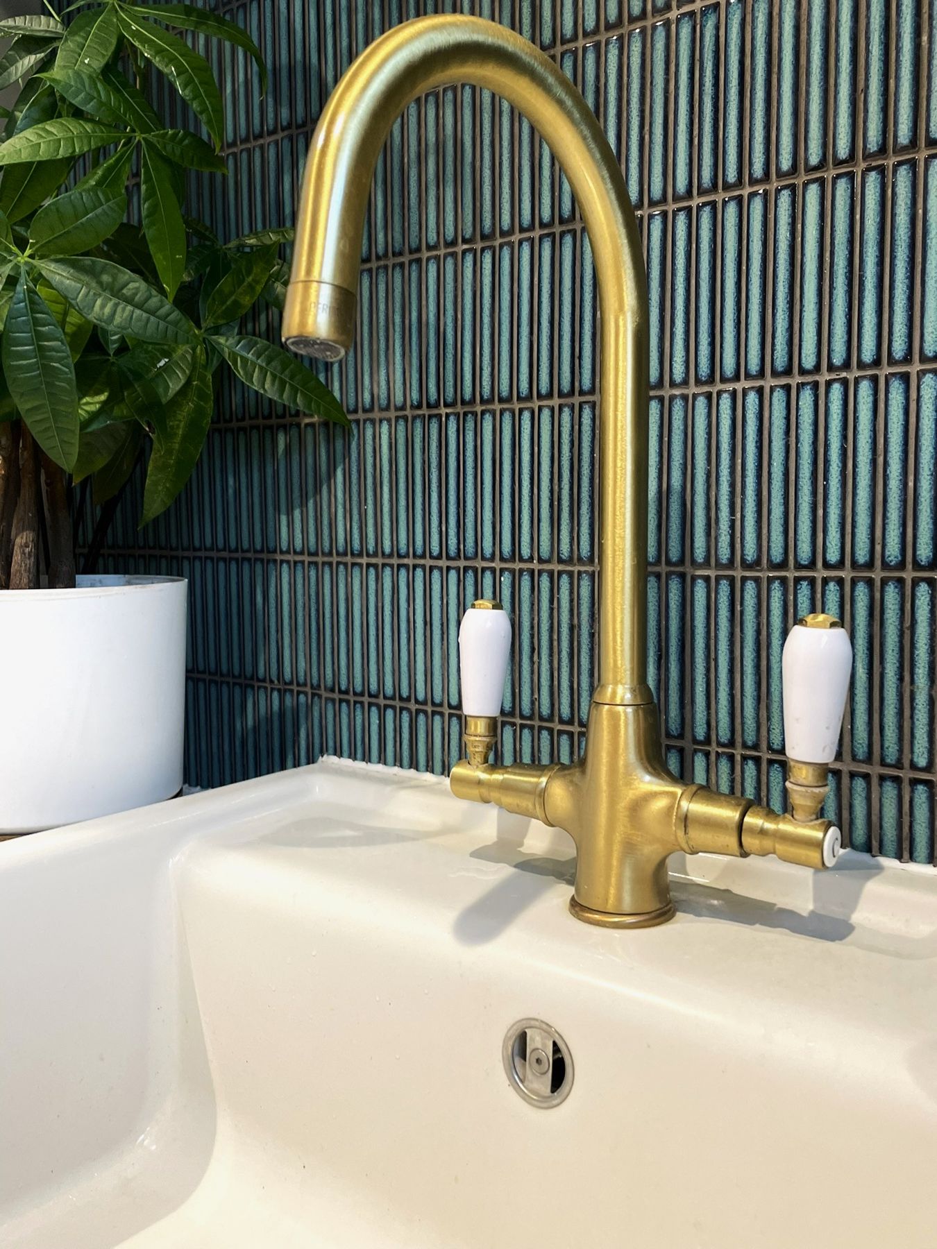 A brass swan-neck tap with white ceramic levers over a ceramic sink