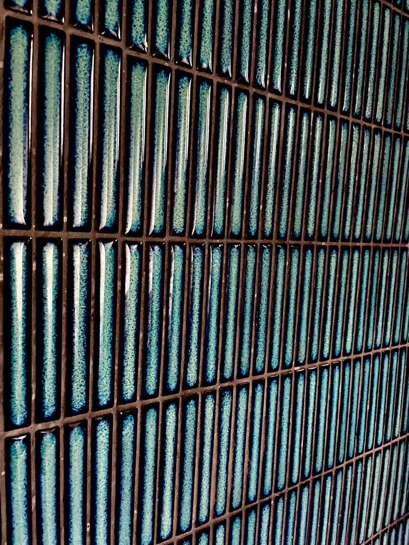 Close-up of glossy teal vertical tiles with dark grout