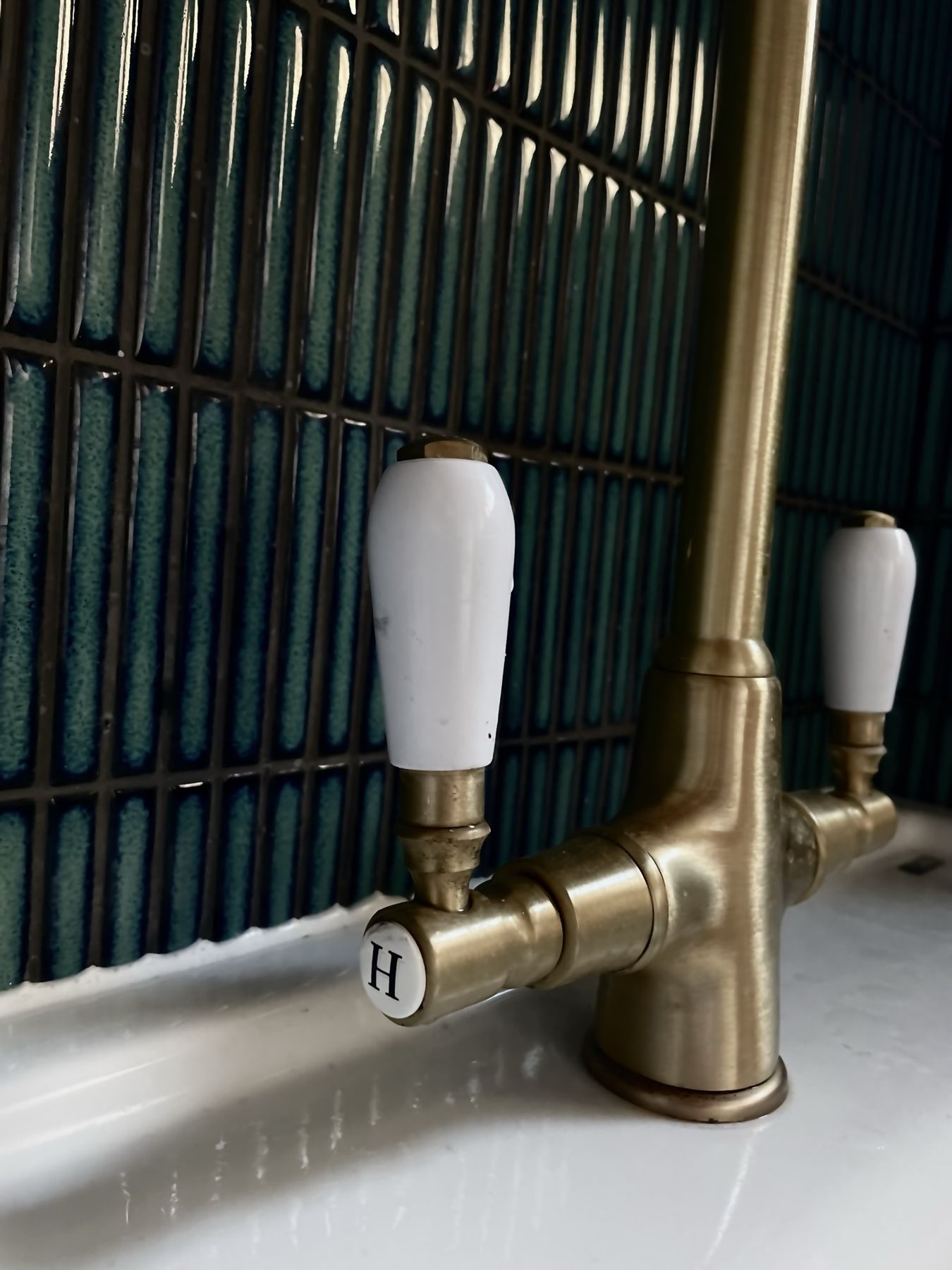 A brass tap with white ceramic levers against teal tiles