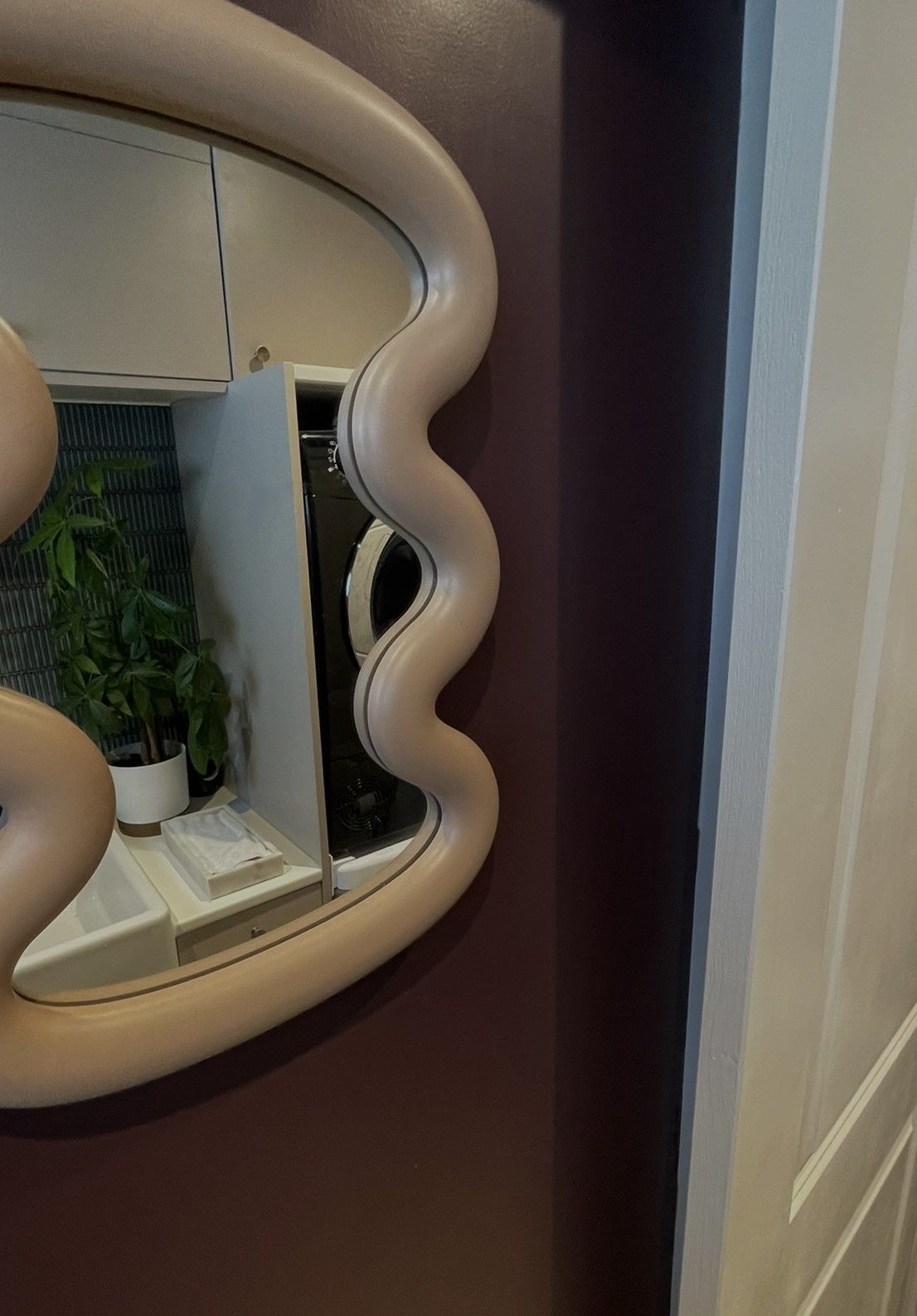 A wavy cream-framed mirror on a plum wall