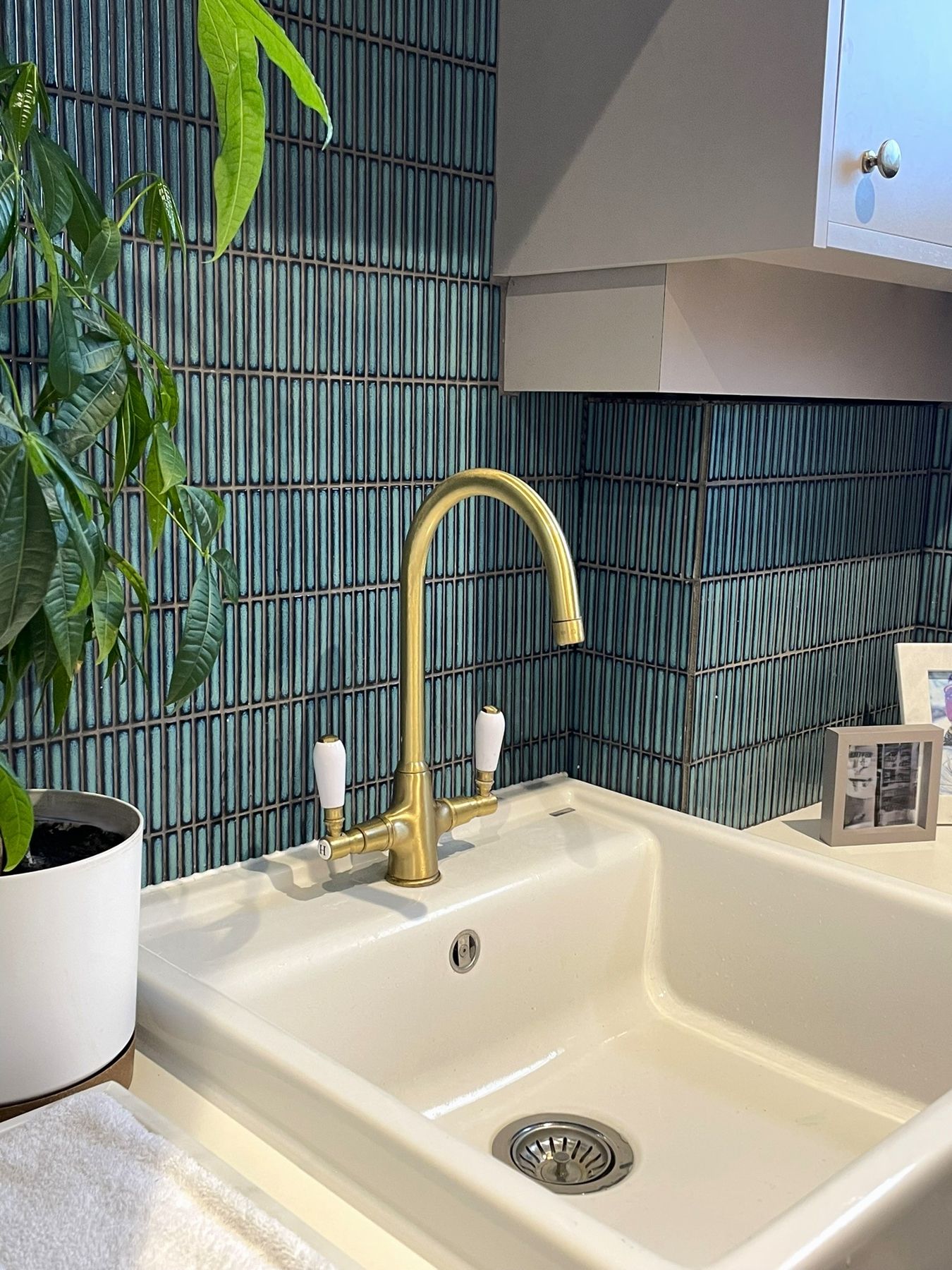 A white ceramic sink with an aged brass swan-neck tap against teal vertical tiles