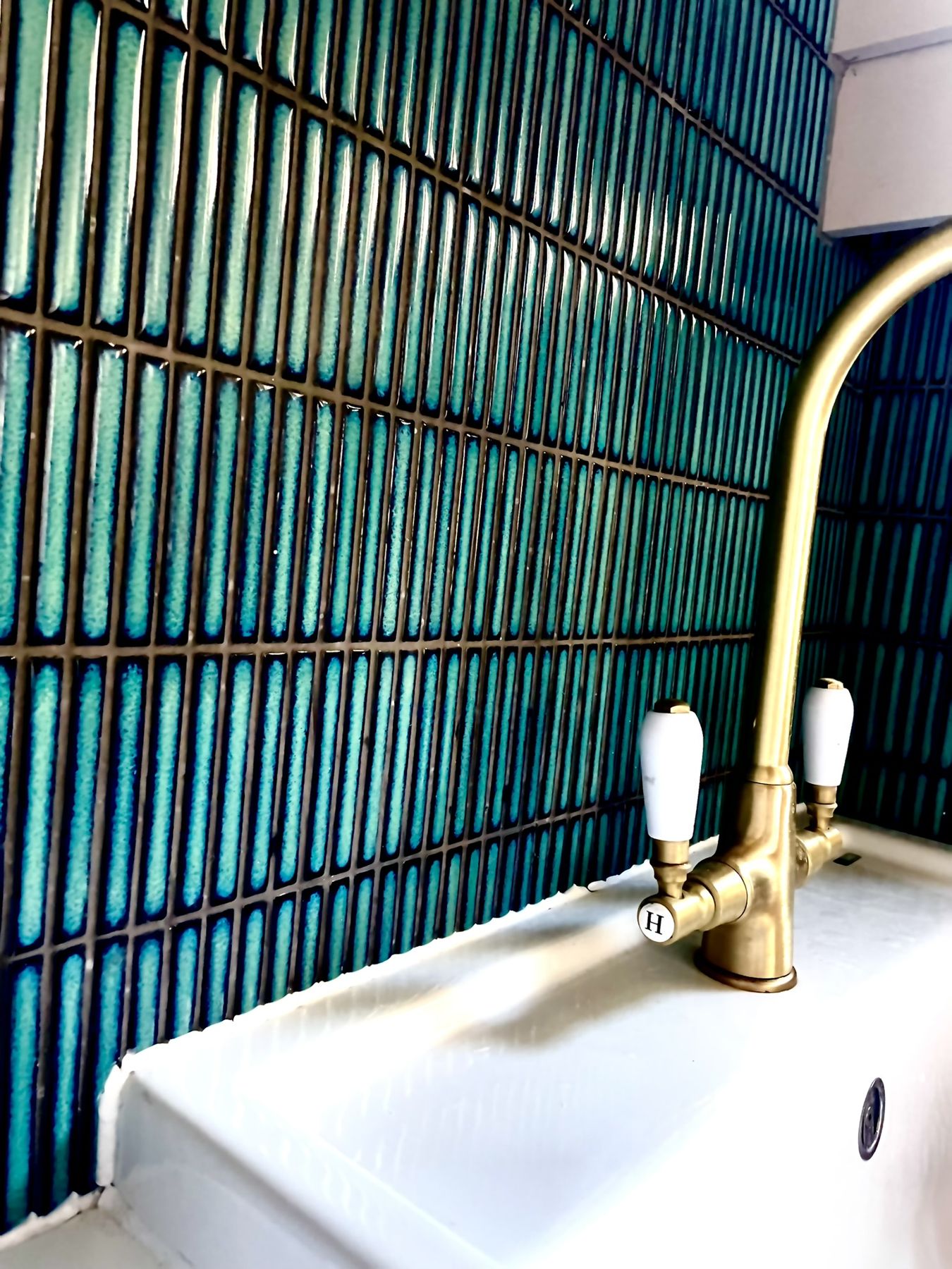A brass tap curving over a white sink against teal tiles