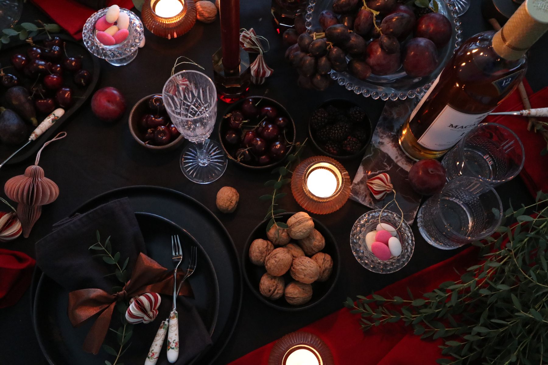 The table from above: dark plates, folded napkins, tealights and fruit
