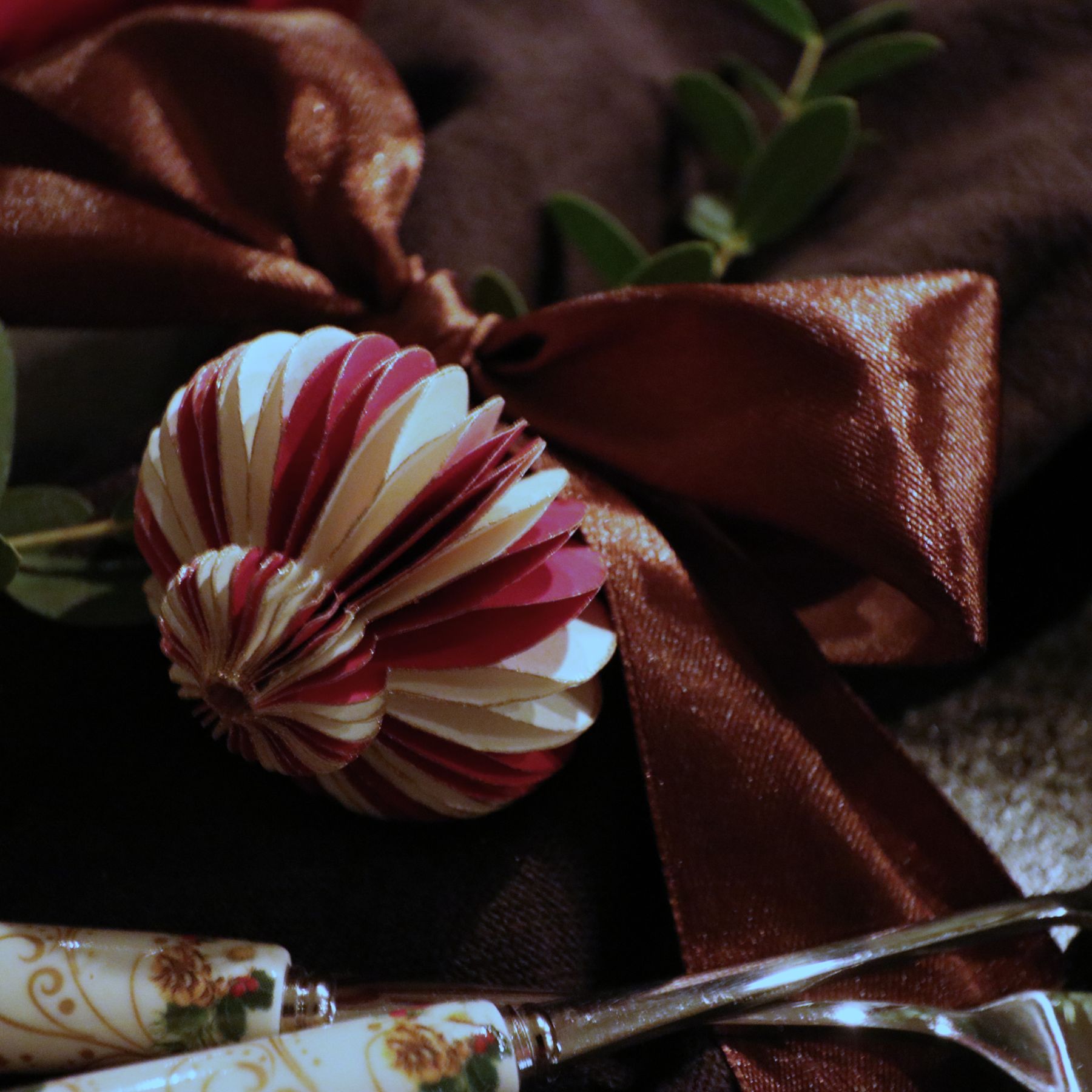 A pink and cream paper bauble tied onto a dark satin napkin