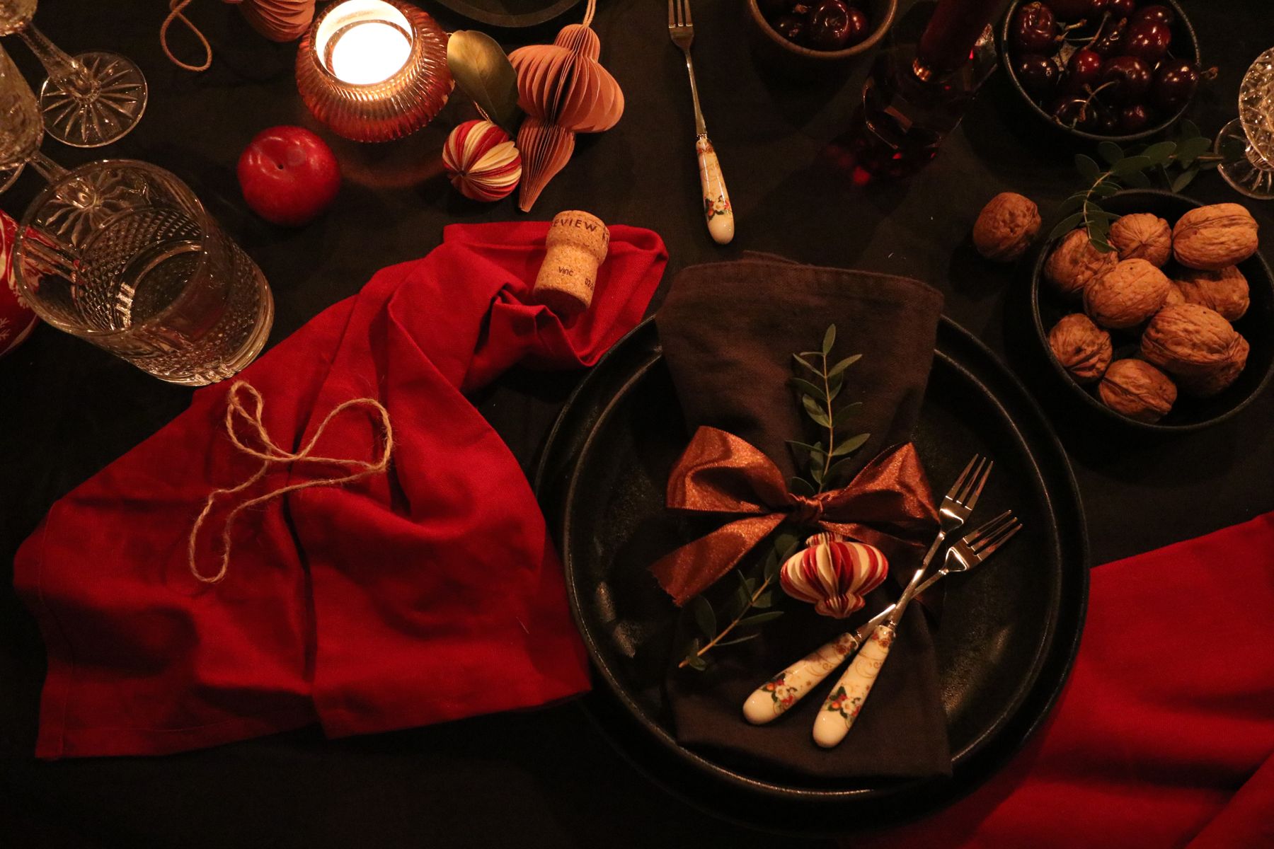 A dark plate with a red napkin, nuts and a sprig of greenery