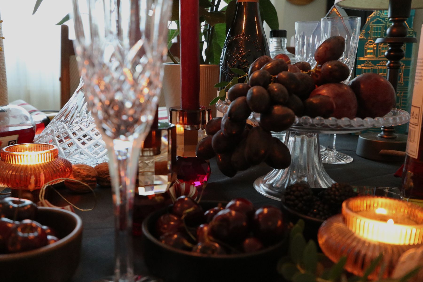 Crystal glasses and a cake stand of fruit lit by candles