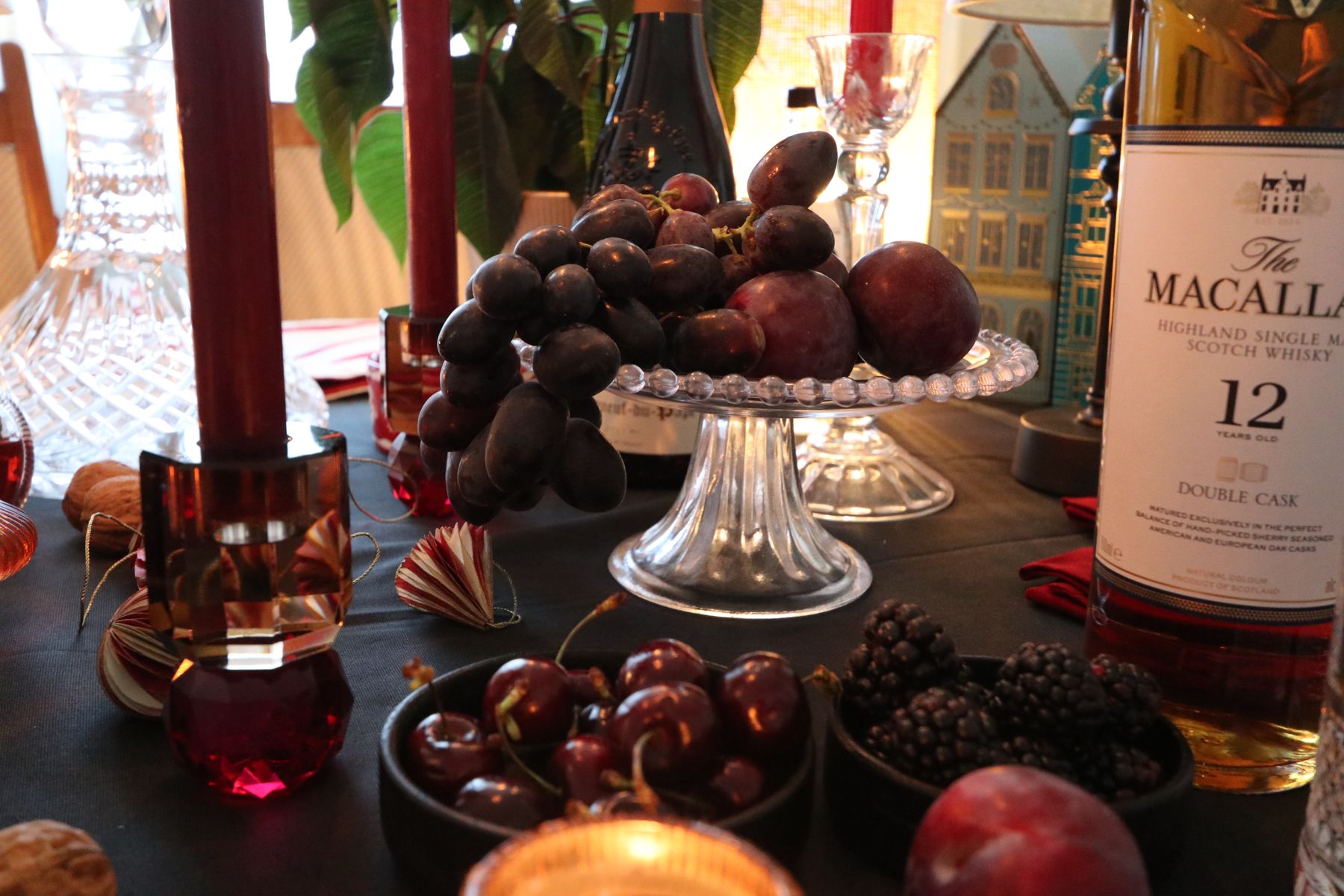 Cut-glass decanters, candles and a bowl of fruit on a dark table